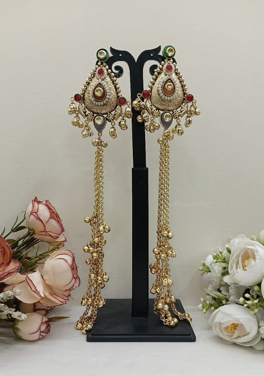 Pair of ornate gold earrings on a black stand with flowers in the background