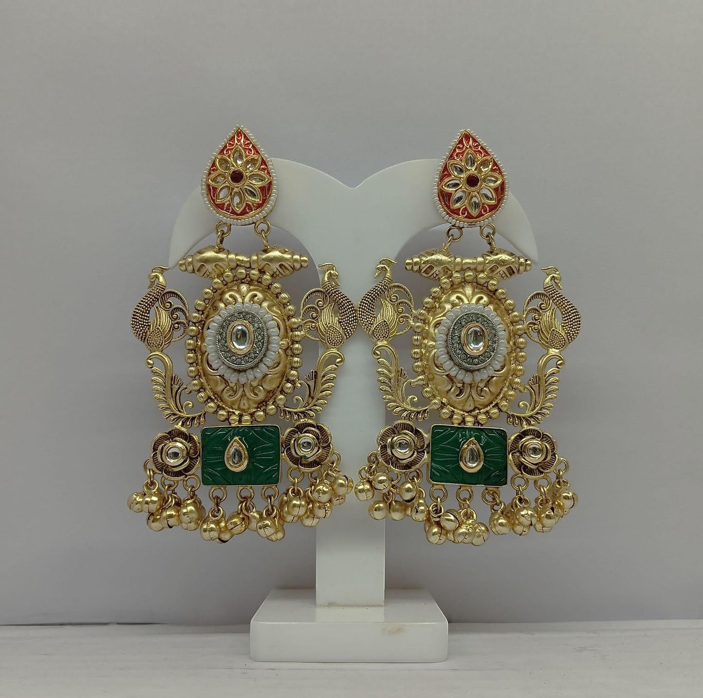 Ornate gold and green earrings on a white stand against a gray background