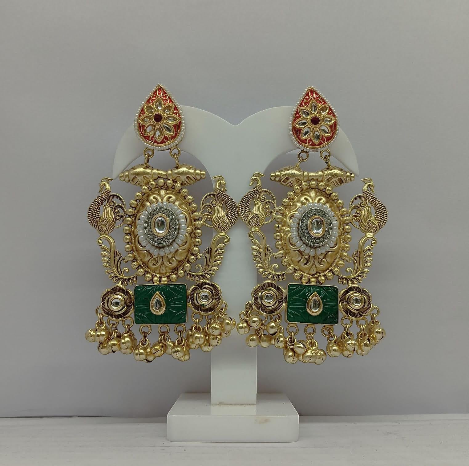 Ornate gold and green earrings on a white stand against a gray background