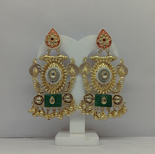 Ornate gold and green earrings on a white stand against a gray background