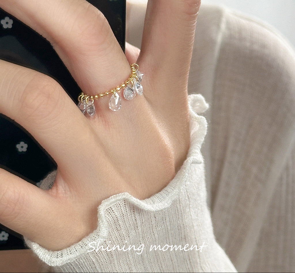 Close-up of a hand wearing a gold ring with clear stones, against a neutral background.