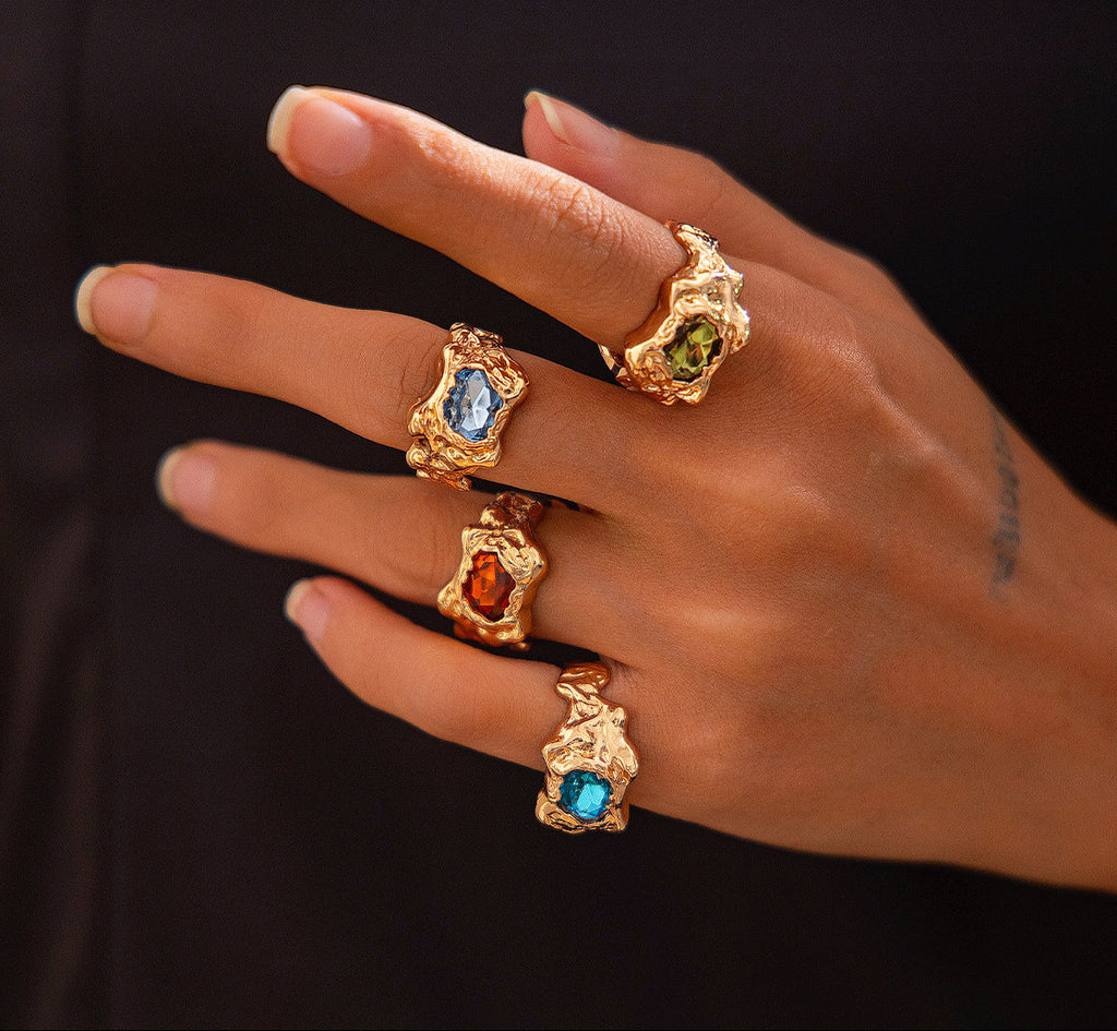 Hand wearing multiple gold rings with gemstones on a dark background