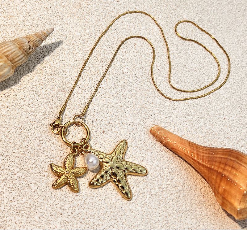 Necklace with starfish and pearl pendant on sand with shells