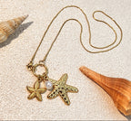 Necklace with starfish and pearl pendant on sand with shells