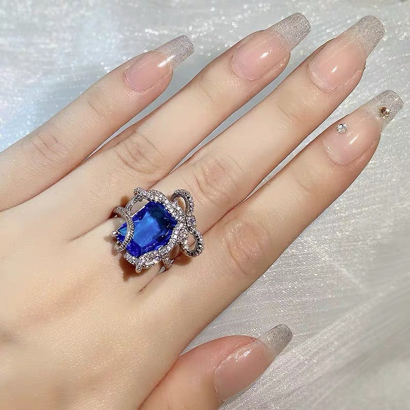 Hand wearing a ring with a blue gemstone on a light background