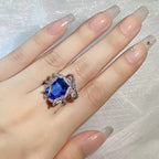Hand wearing a ring with a blue gemstone on a light background