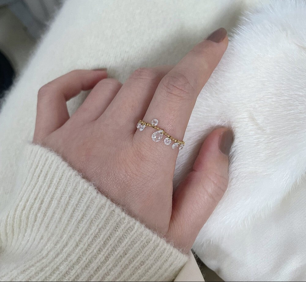 Hand wearing a delicate gold ring with small stones on a white background