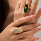 Close-up of a hand wearing two gold rings with green and white stones.