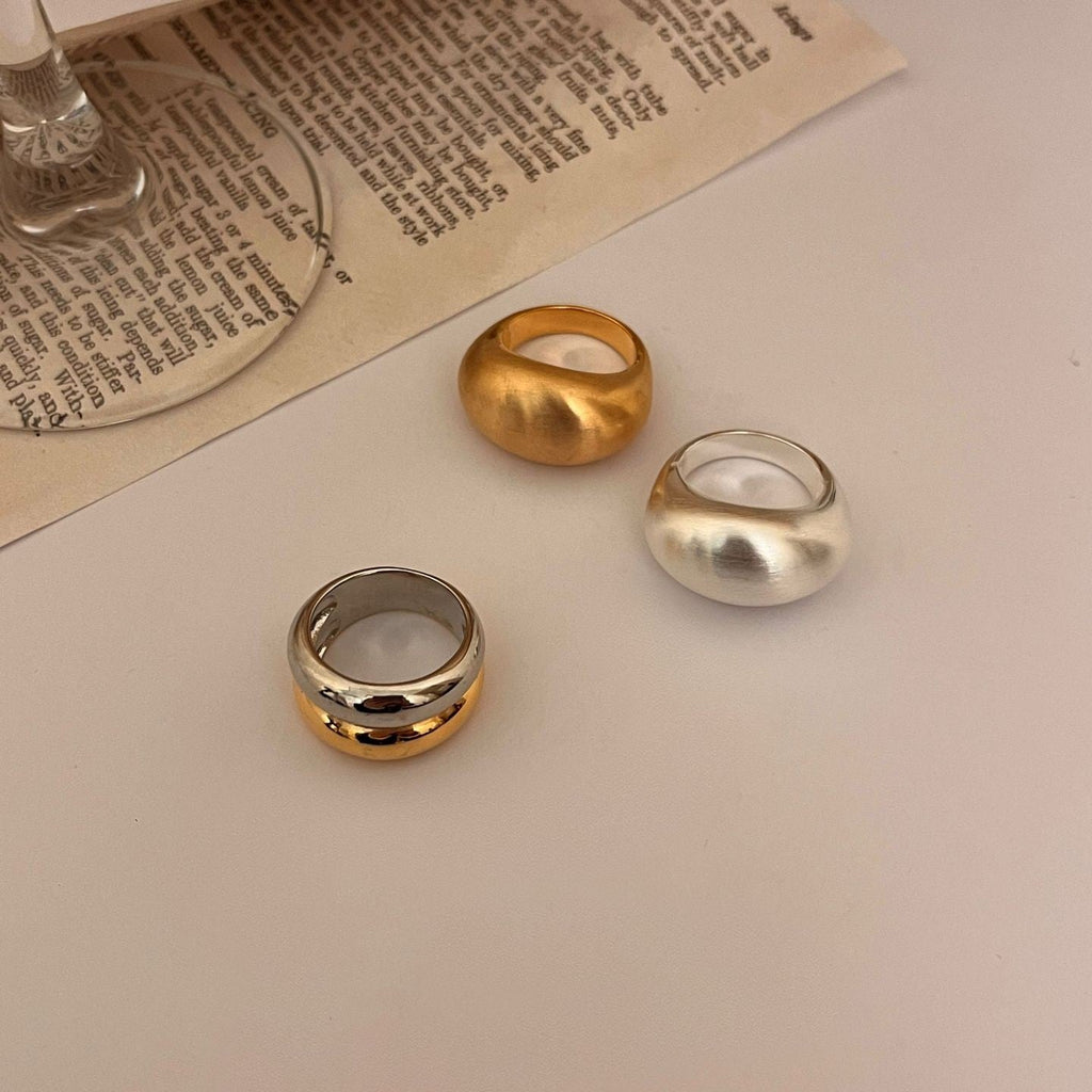 Three rings in gold, silver, and bronze on a textured surface with a book underneath.