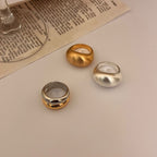 Three rings in gold, silver, and bronze on a textured surface with a book underneath.