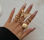 Hand wearing multiple gold rings on a textured beige background