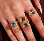 Gold rings with gemstones on a hand against a brown background