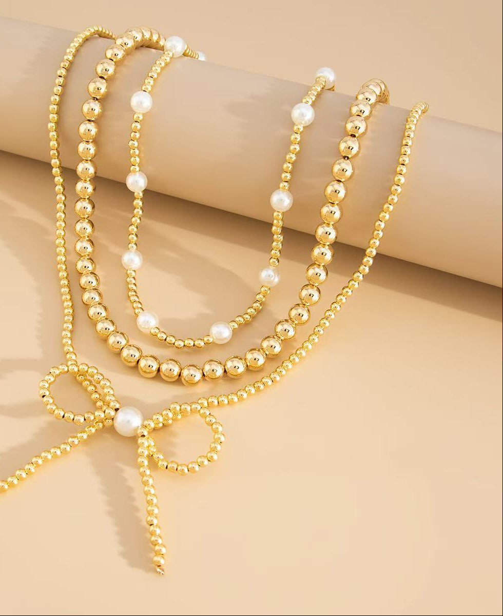 Gold beaded necklace with a bow detail on a beige background