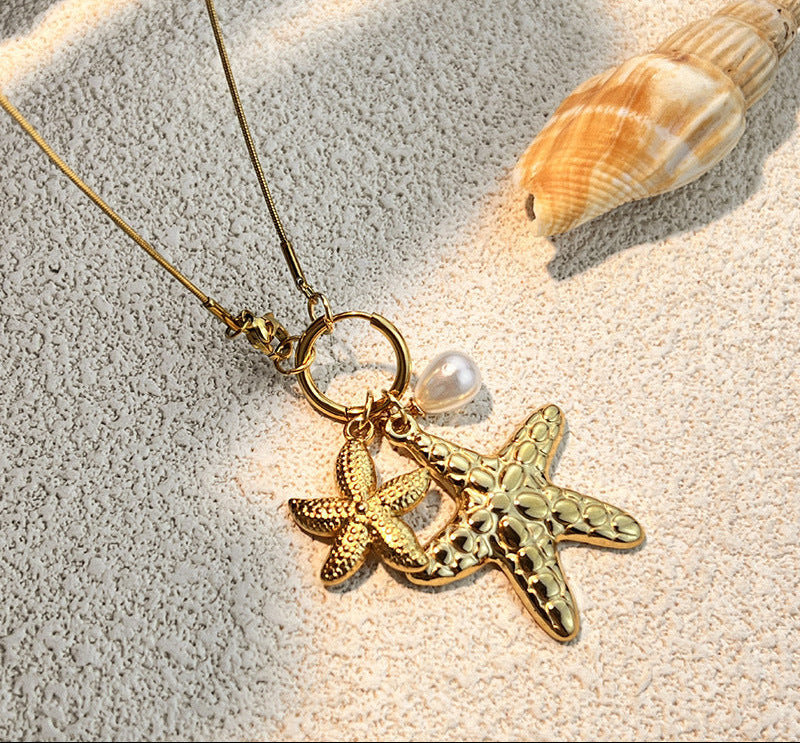 Gold necklace with starfish pendant on sand with shell