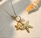 Gold necklace with starfish pendant on sand with shell