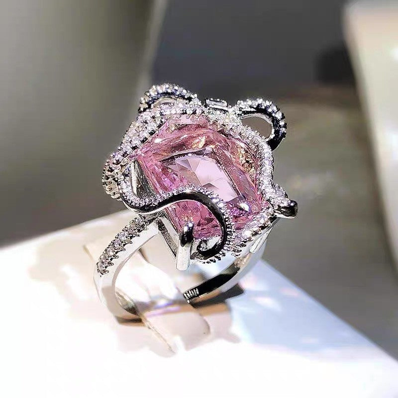Luxury pink gemstone ring with silver and black accents on a reflective surface.