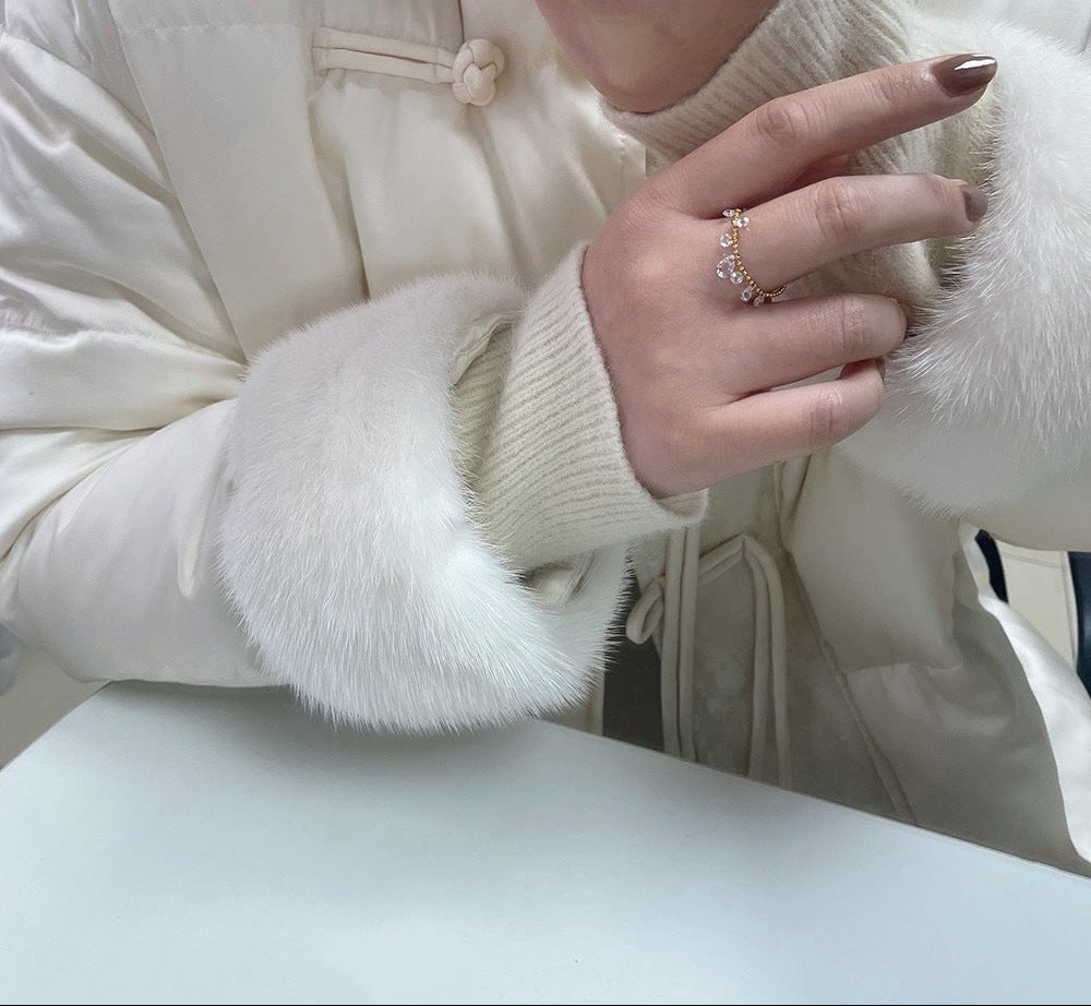 Close-up of a person wearing a white coat with fur-trimmed cuffs and a ring.