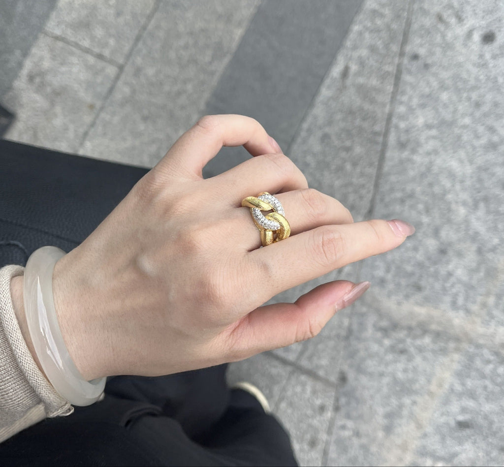 Hand wearing a gold ring with a diamond on a gray pavement background