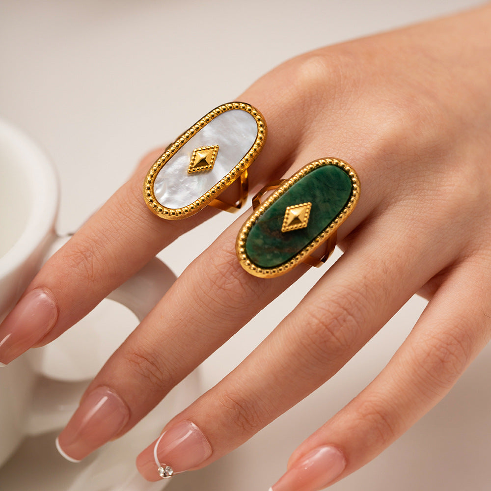 Hand wearing two rings with green and white stones on a neutral background