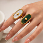 Hand wearing two rings with green and white stones on a neutral background
