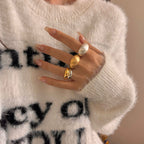 Close-up of a hand wearing two rings with a white sweater in the background