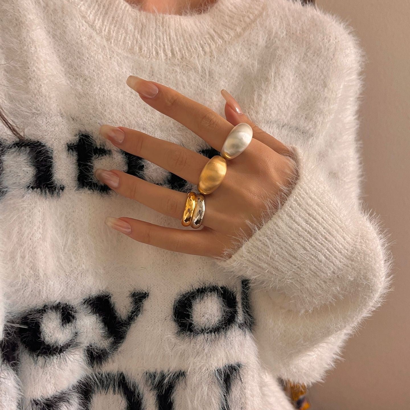 Close-up of a hand wearing two rings with a white sweater in the background