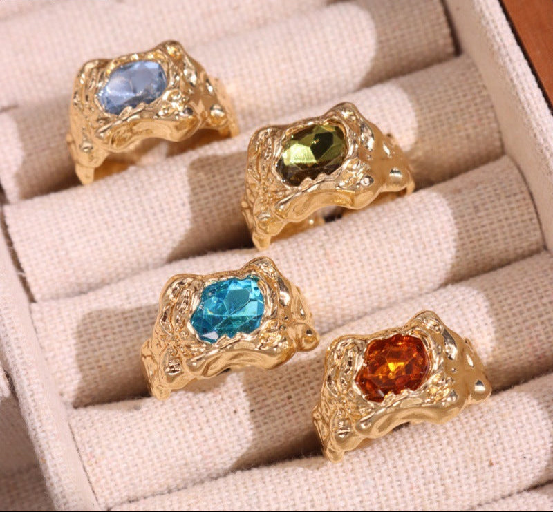 Four gold rings with colored gemstones on a beige fabric surface