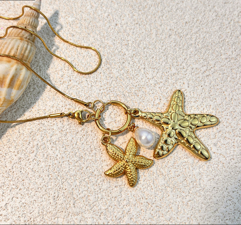 Gold necklace with starfish and pearl charms on a sandy background