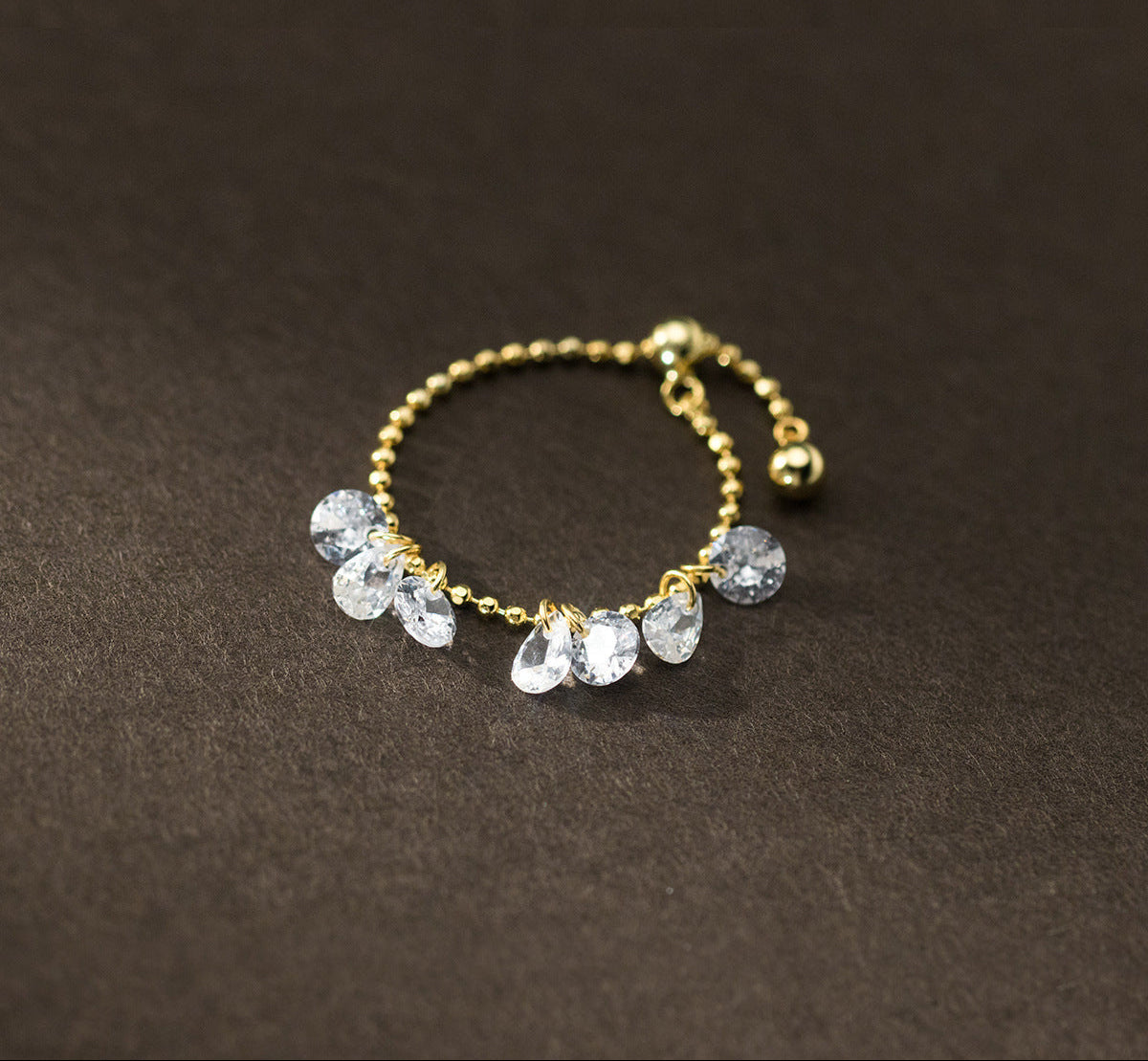 Gold ring with clear gemstones on a dark brown background