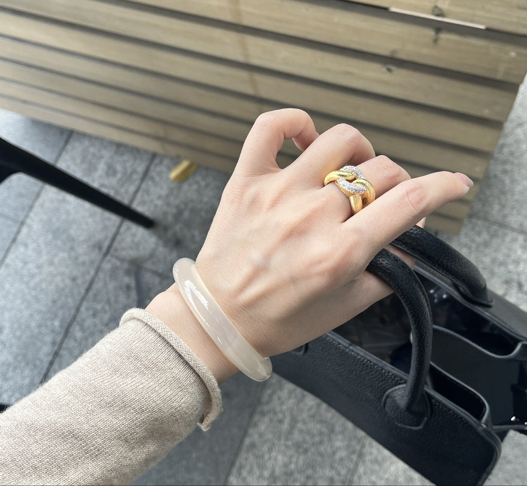 Hand wearing a gold ring on a blurred outdoor background