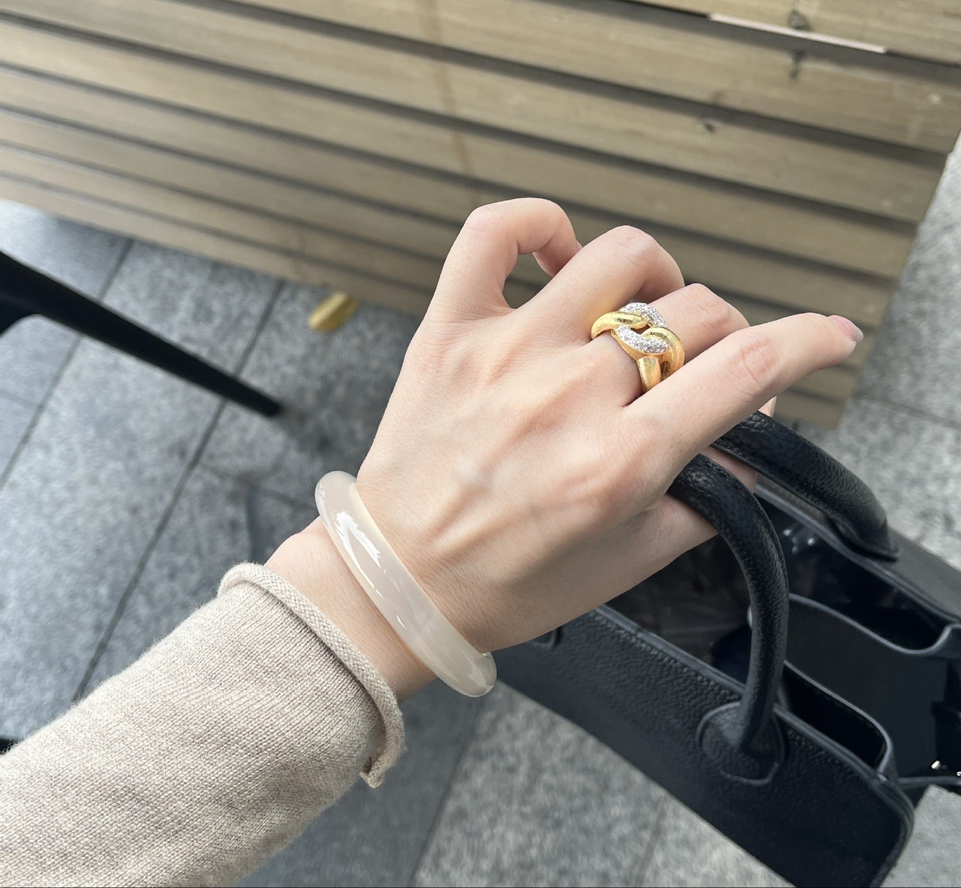Hand wearing a gold ring on a blurred outdoor background