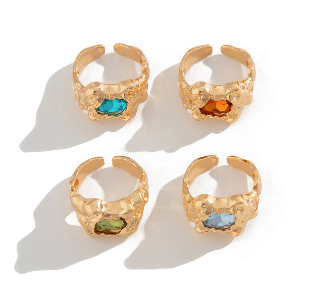 Four gold-rimmed rings with colored gemstones on a white background